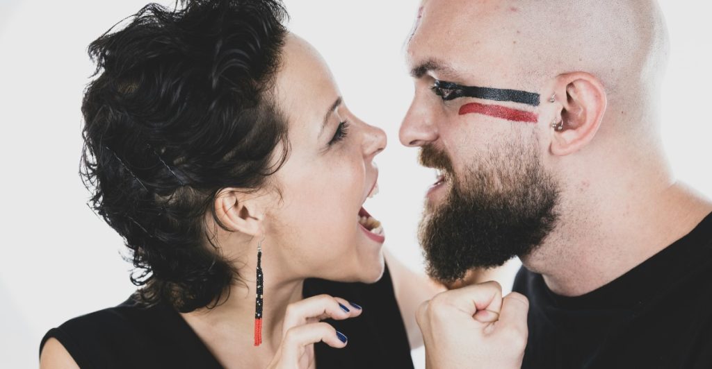A man with face paint and a beard is yelling face to face with a woman who is also yelling.