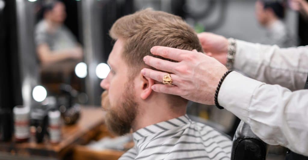 A man getting a haircut at a barbershop with a barber's hands on his head.