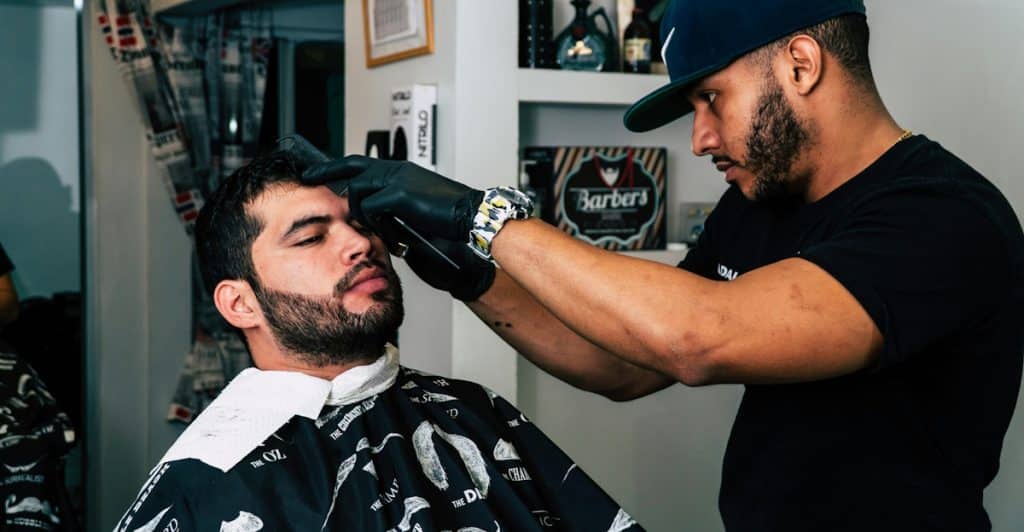 A man getting his eyebrows shaped by a barber wearing gloves at a barbershop.