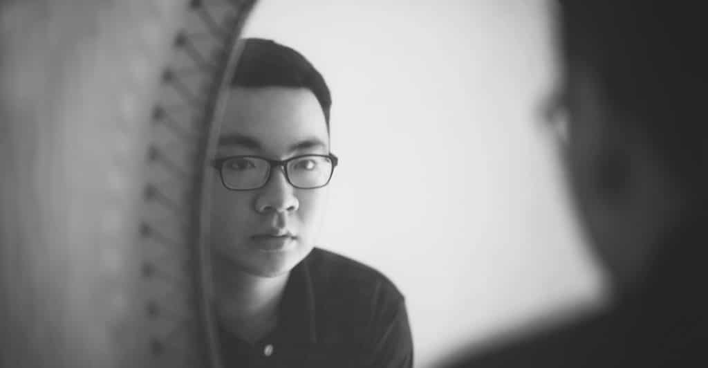 A man in glasses looking intently at his reflection in a mirror.