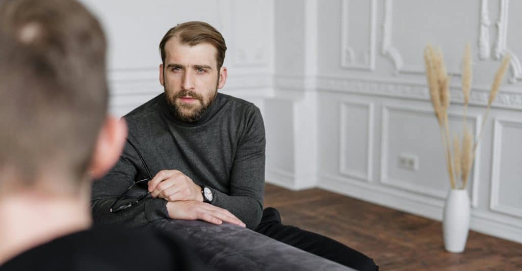 A man sitting on a couch, looking at someone off-camera who is presumably a therapist.