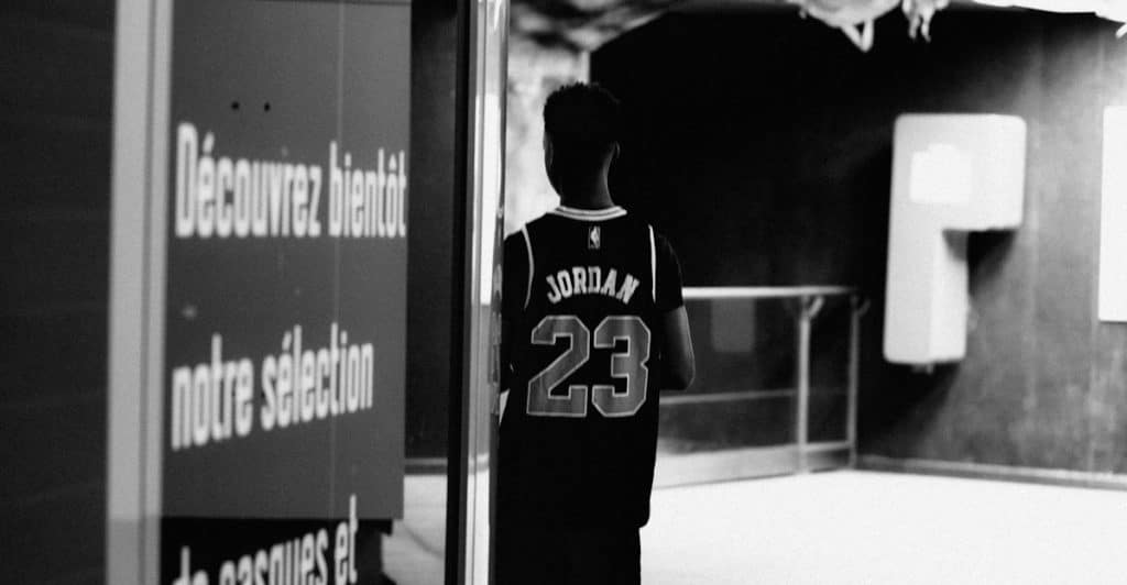 The back of a person wearing a black basketball jersey with "JORDAN 23" on it is visible as they stand in what appears to be a dimly lit hallway.