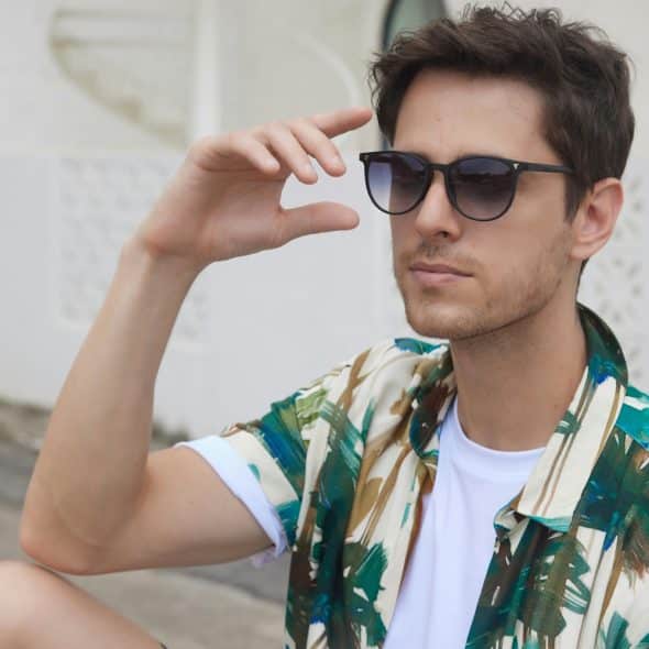 A man wearing sunglasses and a green, blue, and white printed short-sleeve shirt with a white t-shirt underneath.