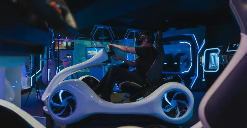 A man wearing a VR headset and sitting in a white futuristic racing simulator with blue glowing accents in a dark room.