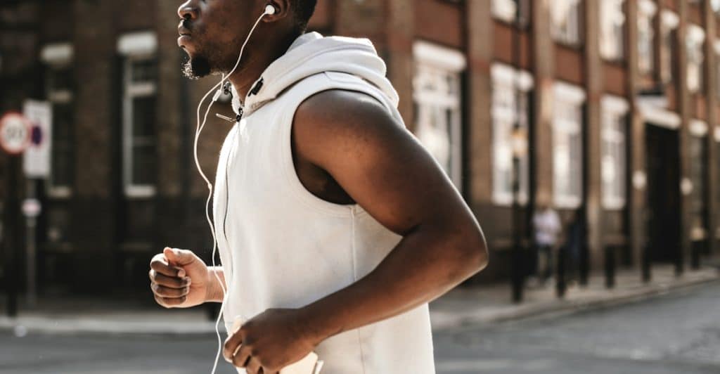 A man jogging outdoors wearing a white hooded vest and white earphones.