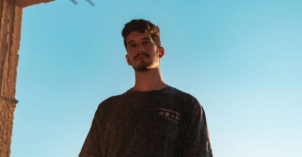 A man with a beard looking up against a clear blue sky, partially framed by a building structure.