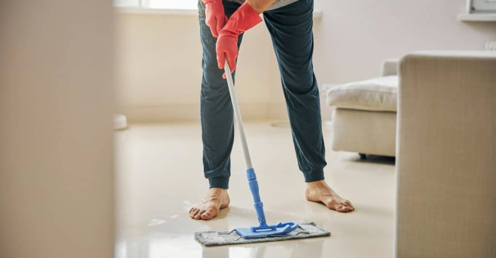 A man in red gloves and a dark outfit using a mop to clean a light-colored floor indoors.