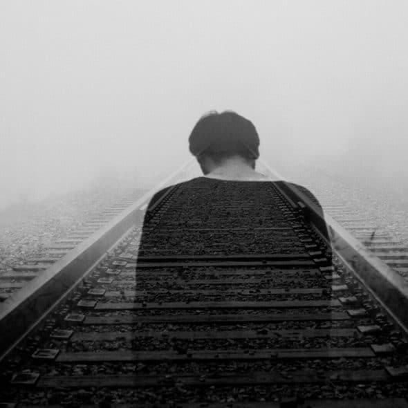 A man standing on railroad tracks that disappear into a foggy distance.
