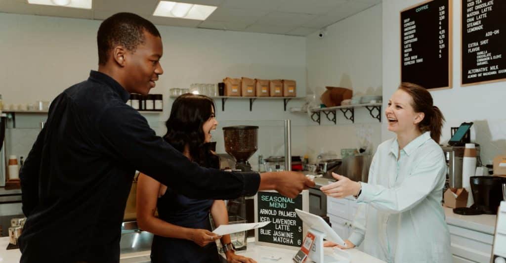 A man handing money to a smiling woman behind a counter, with another woman standing next to him.