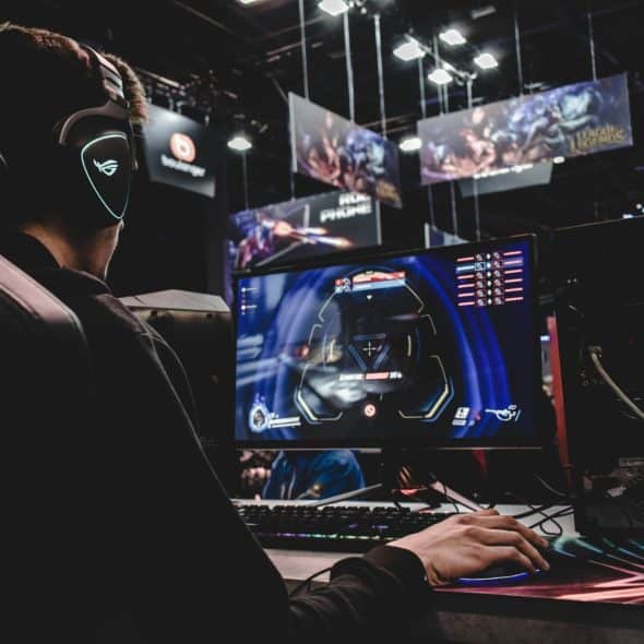A man wearing headphones is sitting in a gaming chair and playing a video game on a monitor.
