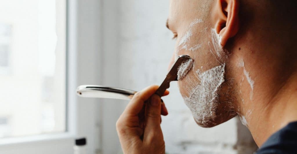 A man shaving the edges of his beard with a straight razor.