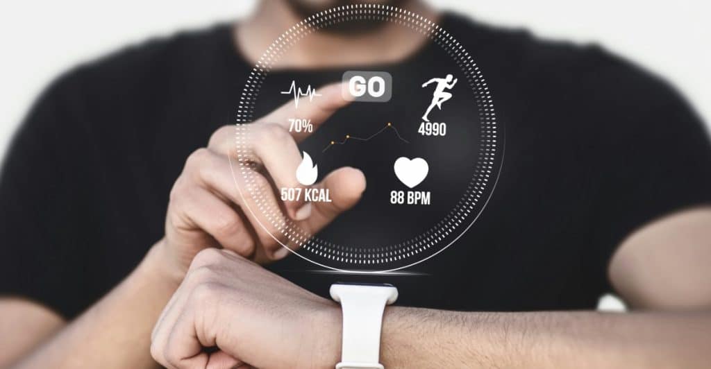 A person's forearm and hand with a white smartwatch on the wrist, reaching out to interact with a futuristic holographic display showing fitness metrics like heart rate and calories burned.