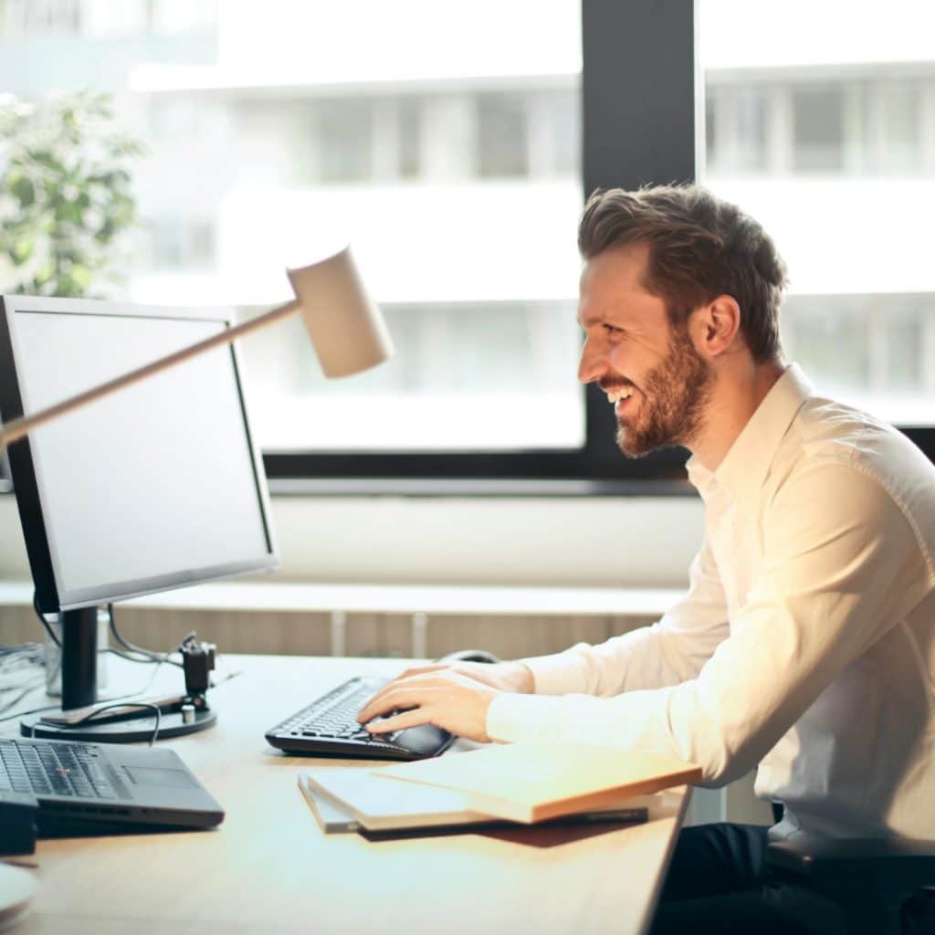 A man smiling and looking at a computer screen while typing on a keyboard.
