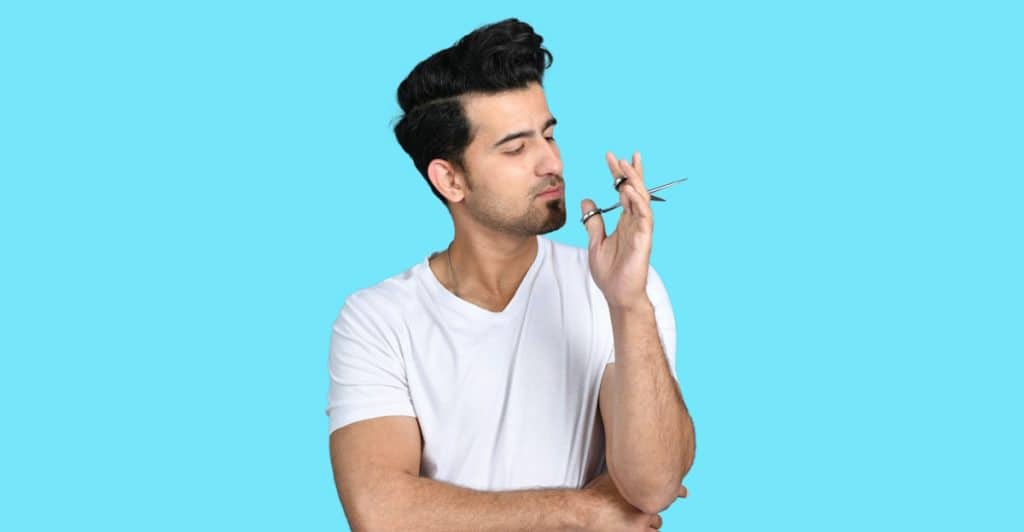 A man in a white t-shirt holding small scissors near his nose, appearing to trim nose hair.
