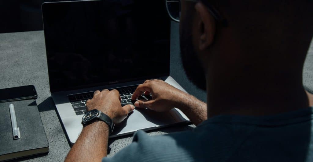 A man typing on a laptop, seen from behind his shoulder, with glasses resting on his head