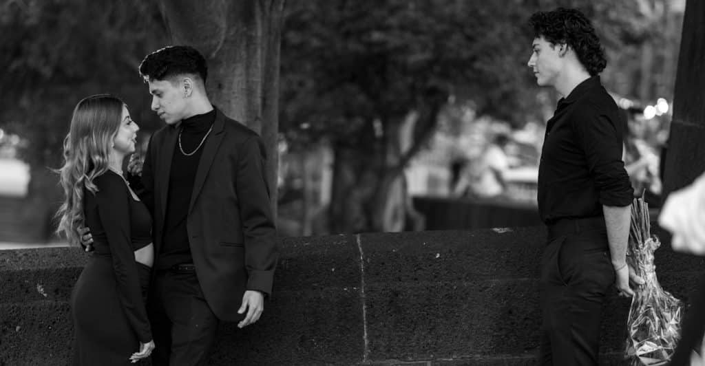 A man standing alone, looking at a couple embracing.