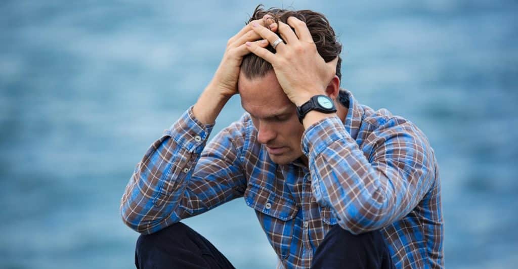 A man sitting down outdoors with his head in his hands, looking distressed.