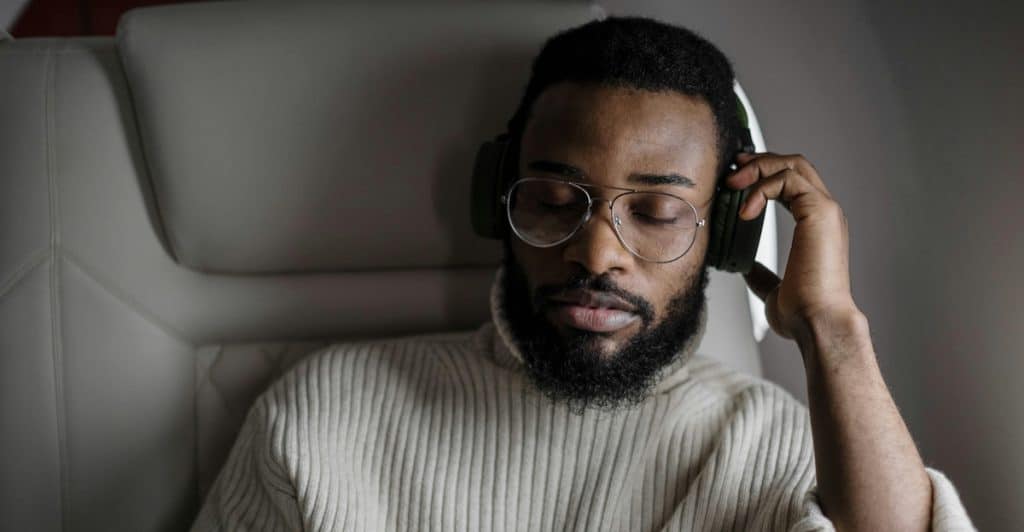 A man wearing glasses and a turtleneck sweater listening with headphones.