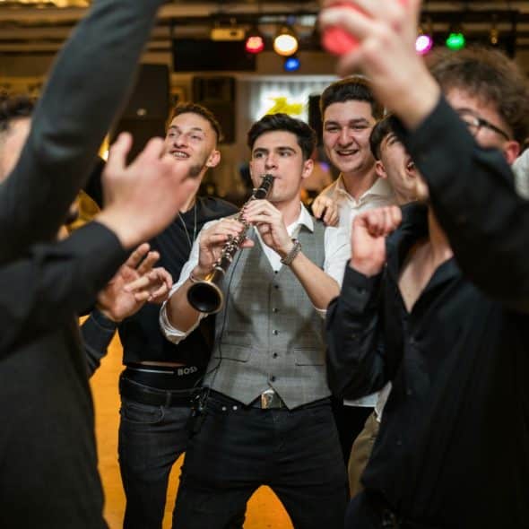 A group of men celebrating around a man playing a clarinet at what appears to be a party or event.