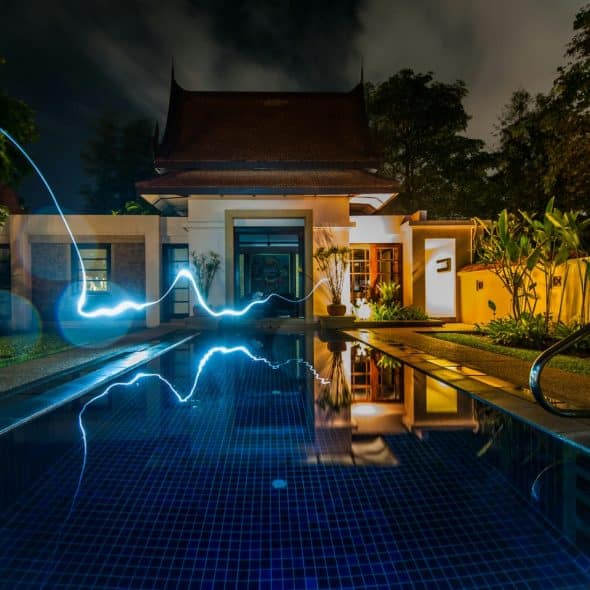 A modern house with a swimming pool at night, featuring a glowing blue light trail over the water.
