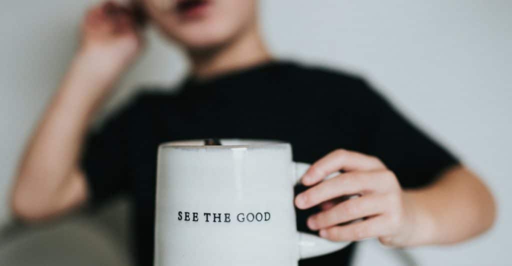 A close-up of a person holding a mug with the words "SEE THE GOOD" printed on it.