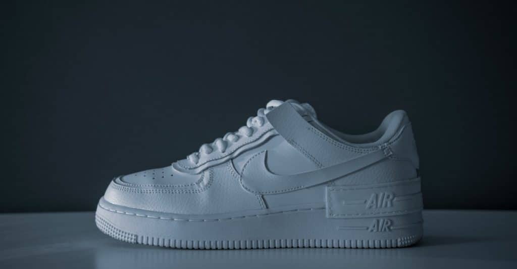 A clean, all-white Nike Air Force 1 sneaker displayed against a dark background.