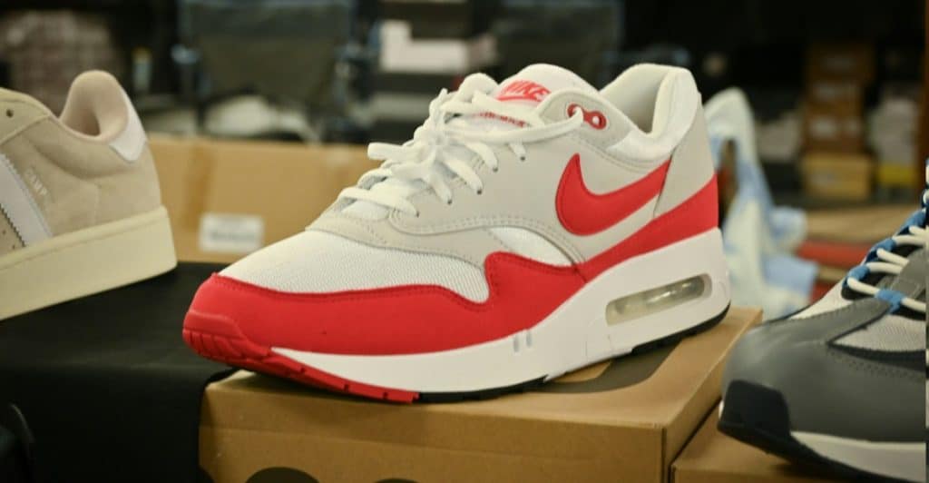 A red and white Nike Air Max 1 sneaker with a visible air unit in the sole, resting on a cardboard box.