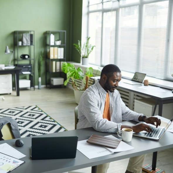 A neatly organized desk featuring a desktop computer with multiple screens, a keyboard, a mouse, and two green potted plants, suggesting a productive workspace.