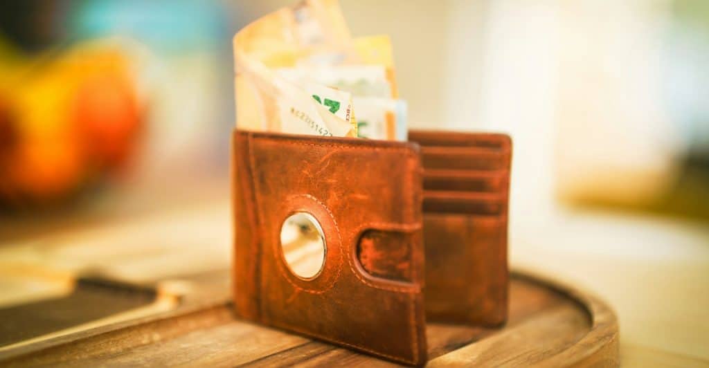 A brown leather wallet is open, with several banknotes sticking out of it, sitting on a wooden surface.
