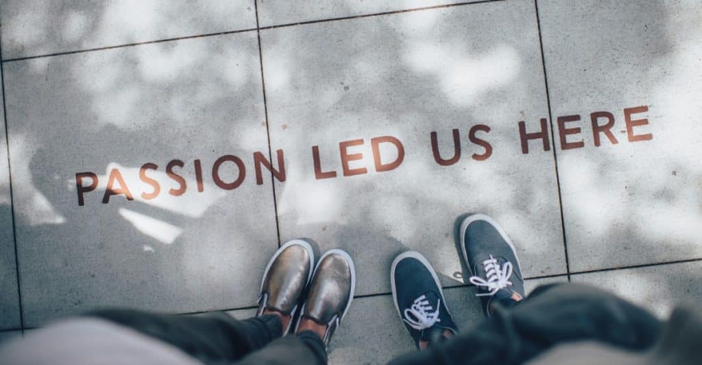 The phrase "PASSION LED US HERE" inscribed on a stone ground, with the feet of two people visible at the bottom of the frame.