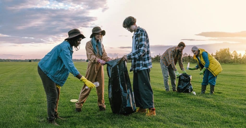 Five people picking up trash in a field with bags and gloves