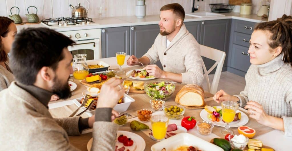 A group of four people seated around a dining table, eating and conversing, with plates of food and drinks in front of them.