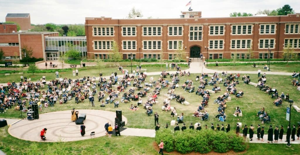 A large group of people gathered on a green lawn in front of a brick building.