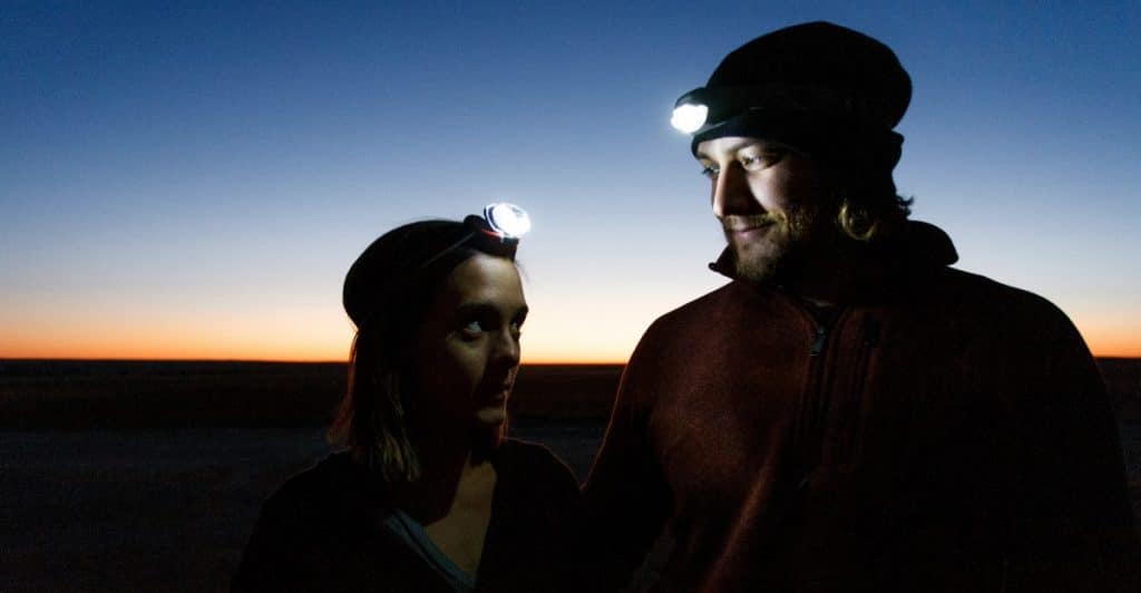 A man and a woman standing together outdoors at dusk, both wearing headlamps that illuminate their faces.