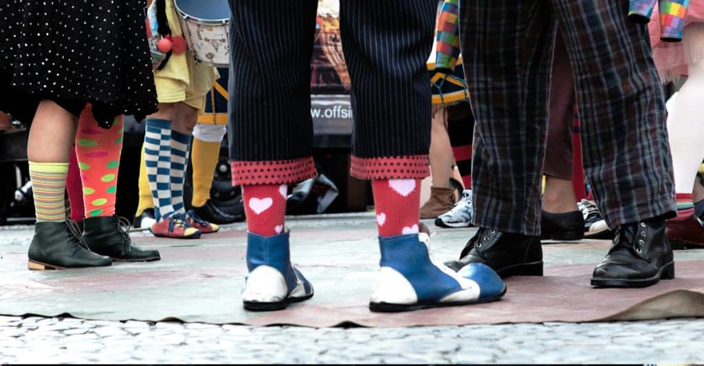The lower legs and feet of several people are shown, with some wearing brightly colored and patterned novelty socks with various shoes.