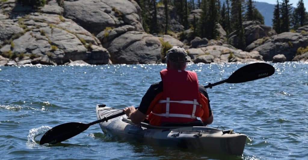 A person kayaking on a lake surrounded by rocks and trees.