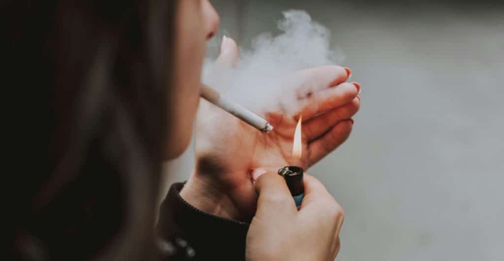 A person lighting a cigarette with smoke visible.