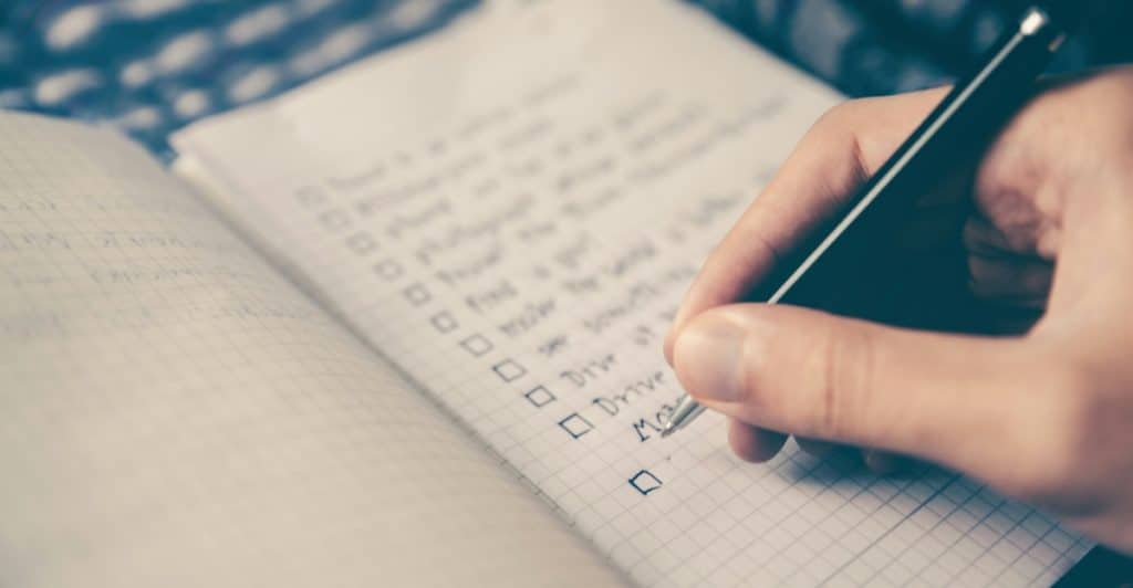 Close-up of a person's hand making a checklist with checkboxes in a notebook.