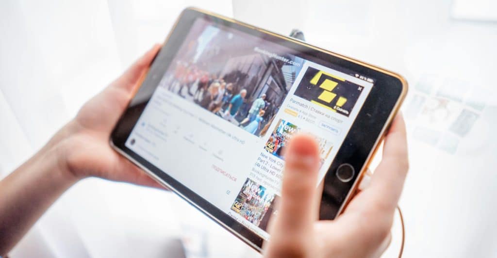 A person is holding a gold and white tablet horizontally, watching a video on YouTube, with their fingers visible on the sides of the device.