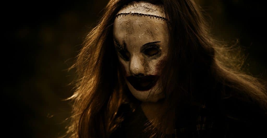 A person with long brown hair wearing a white and black mask with stitches.