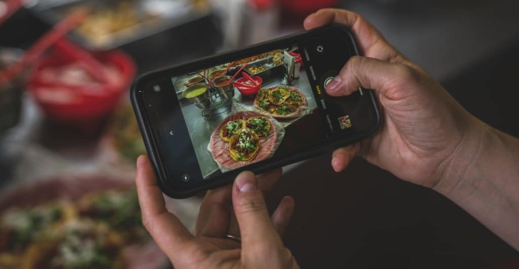 Hands holding a smartphone taking a picture of two plates of colorful street food.