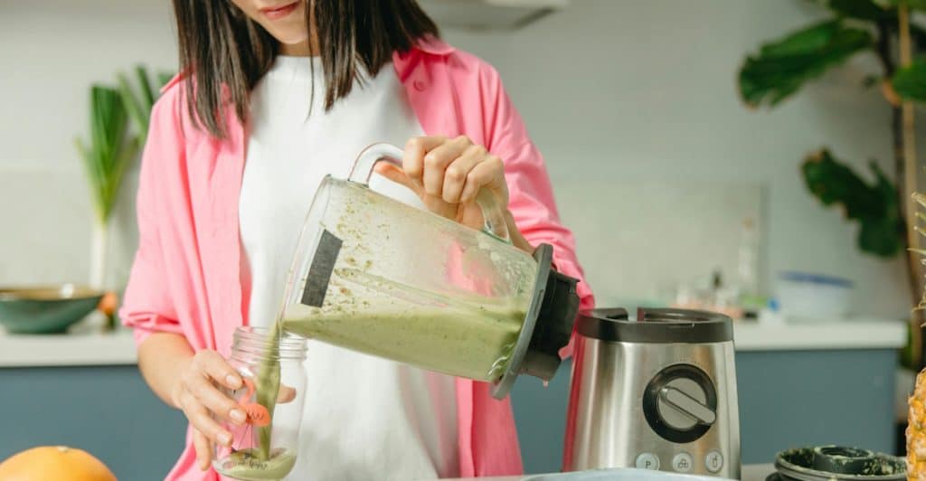 A person pouring a green liquid from a blender into a glass jar.