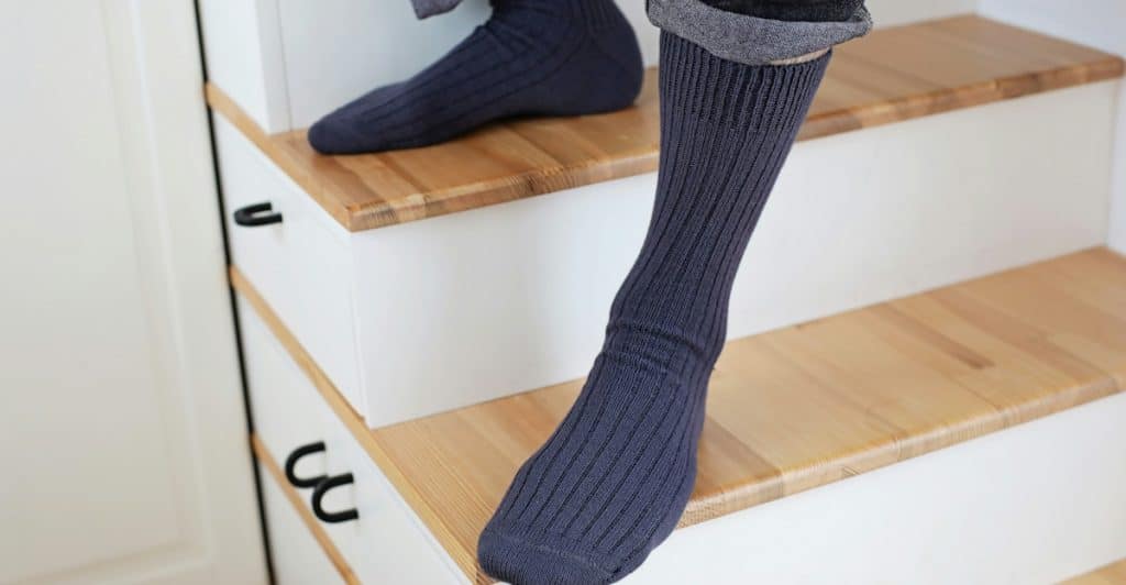 A person's lower legs and feet are visible, wearing dark socks while standing on wooden stairs.