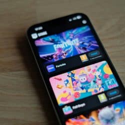 A smartphone showing the Epic Games store with "Fortnite" and "Fall Guys" game listings prominently displayed on a wooden surface.