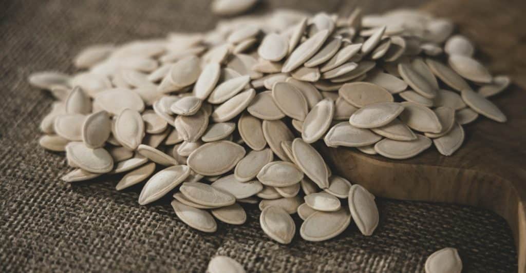 A pile of shelled pumpkin seeds scattered on a piece of brown burlap fabric and a wooden board.