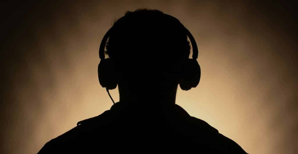 A dark silhouette of a person from the shoulders up, wearing headphones against a warm, gradient background.