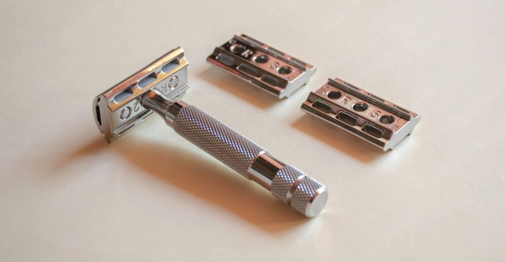 A silver safety razor disassembled, with its handle and two razor heads displayed on a light surface.