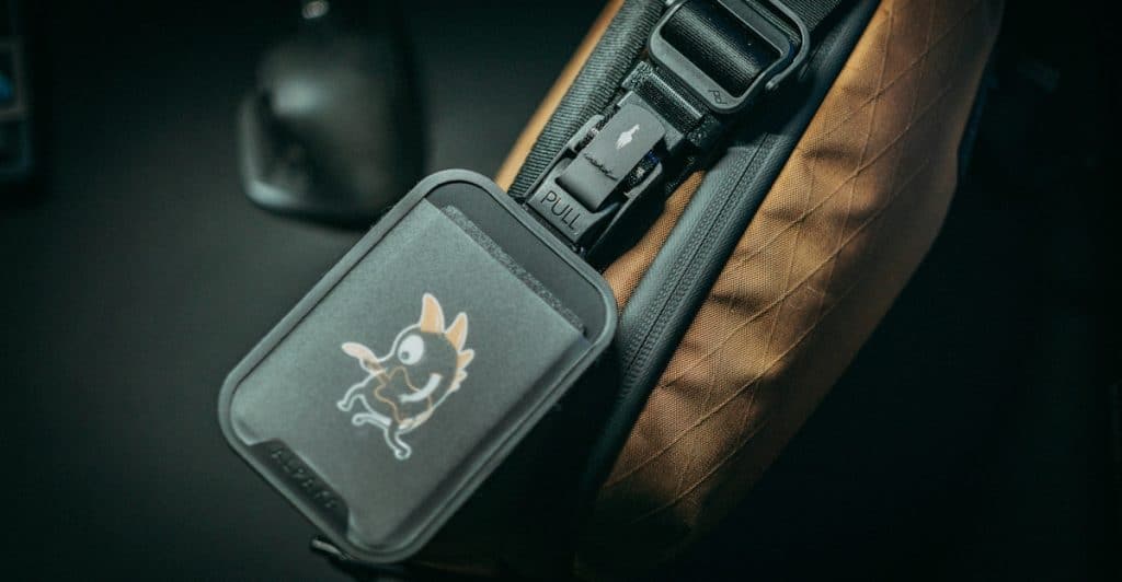 A smart tracker device with a cartoon image is clipped to a bag, next to a computer mouse.