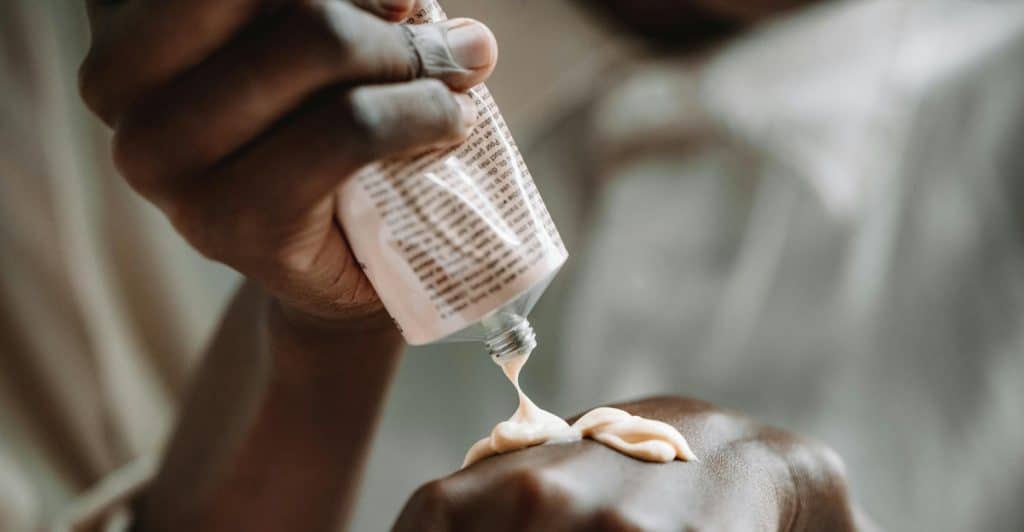 A close-up of lotion being squeezed from a tube onto the back of a hand.