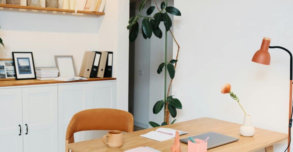 A stylish home office setup with a wooden desk, a plant, and an orange lamp, next to a white cabinet